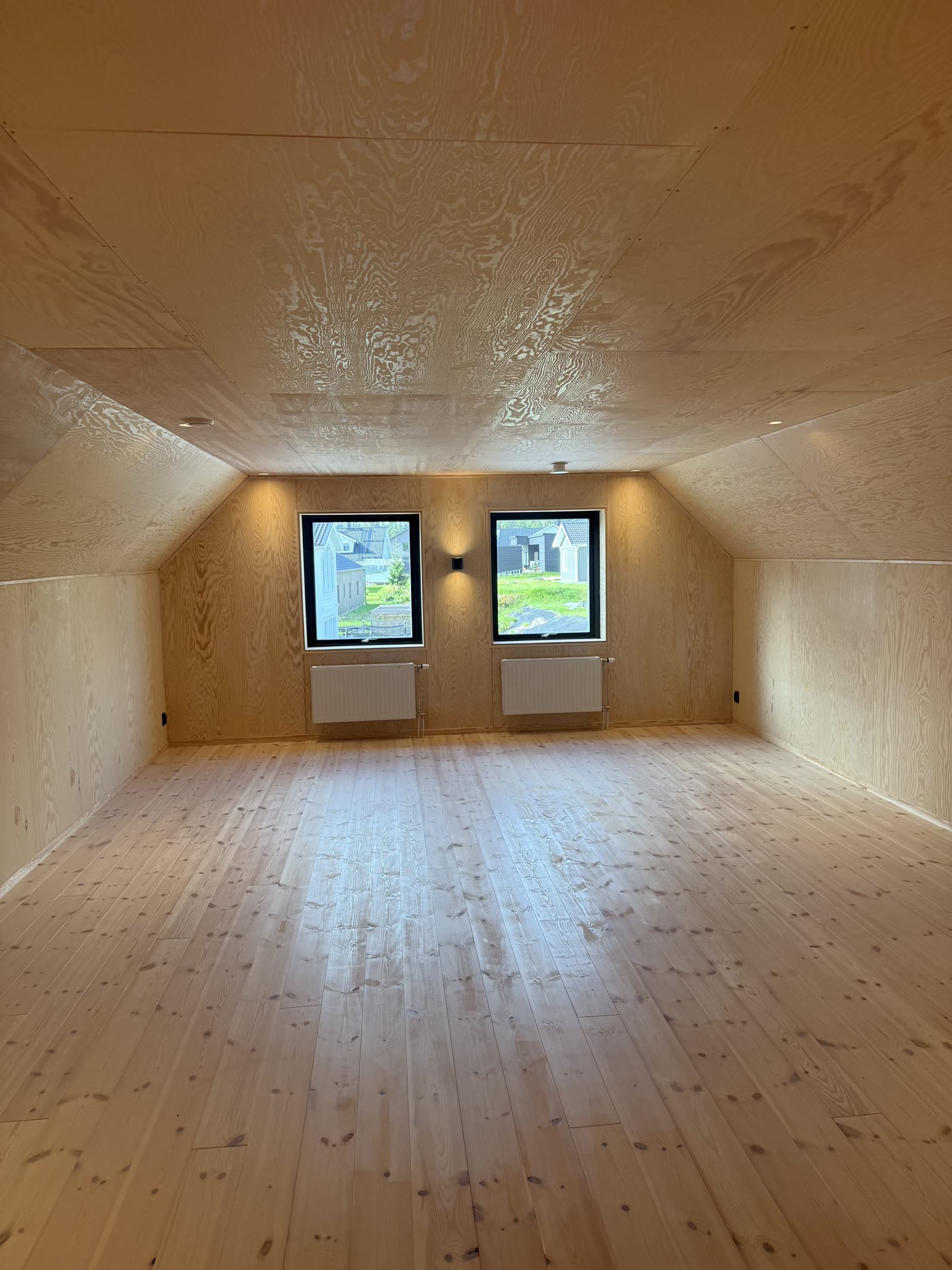 Färdigt rum med trägolv, plywoodpanel och Plejd-belysning i fönsternischen