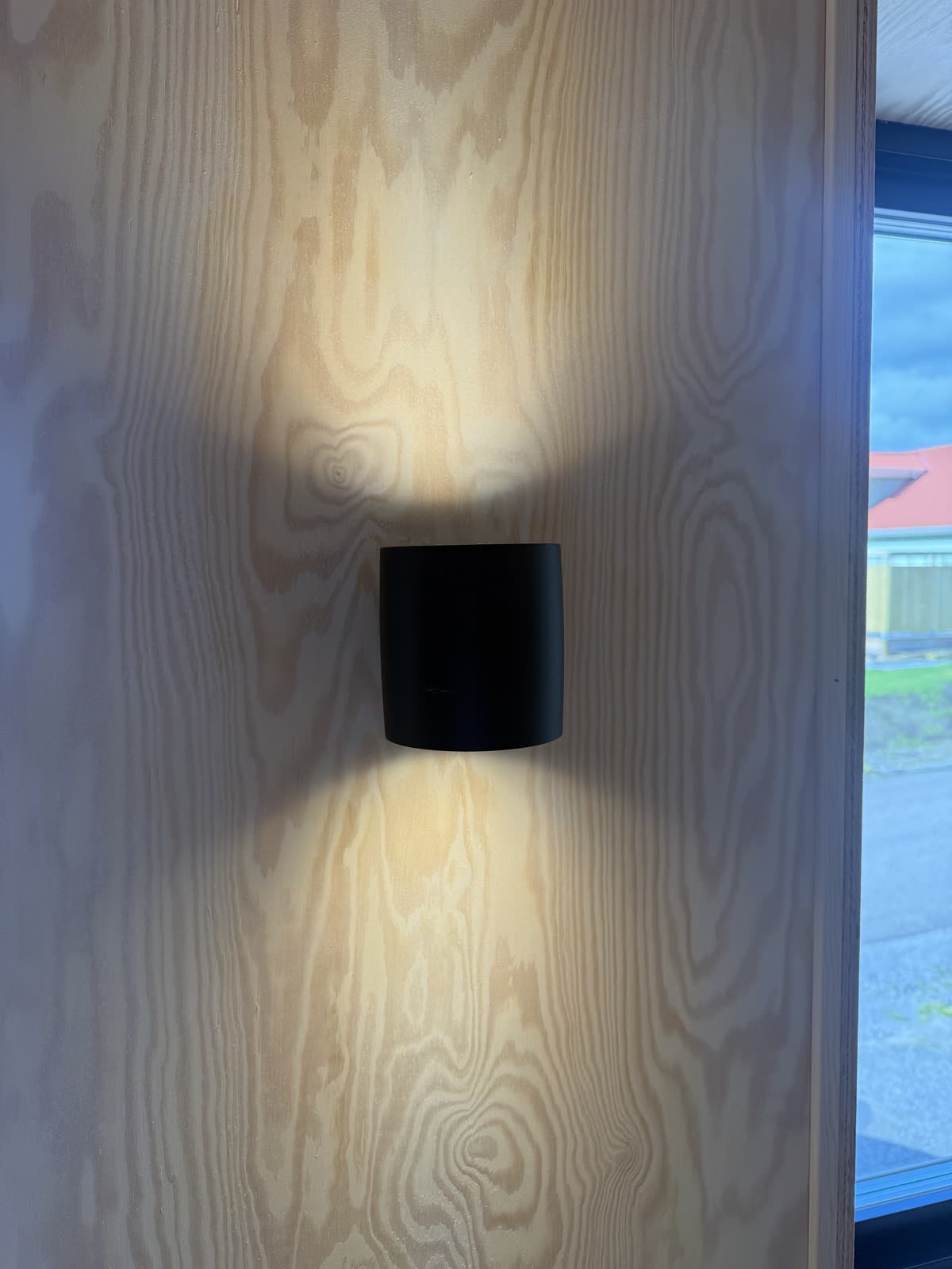 Plejd väggarmatur OUT-01 i svart monterad på plywoodväggen